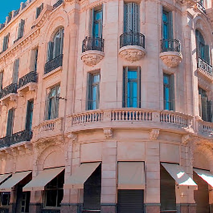 Esquina de un edificio neoclásico con balcones de hierro, balaustrada y toldos en la planta baja.